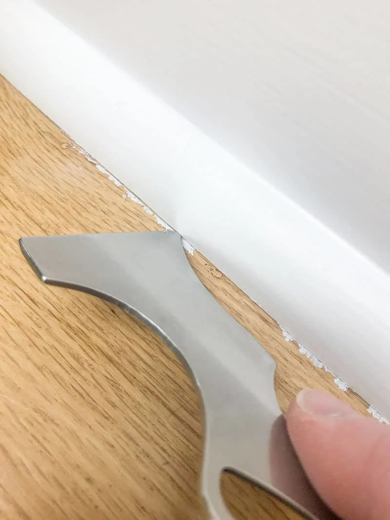 scoring seam between baseboards and floor with painter's tool