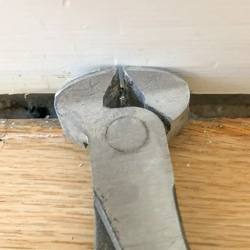 nail puller clamped around base of nail in baseboards