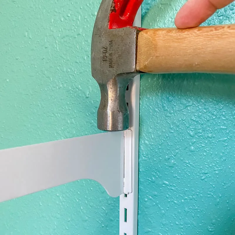 hammering shelf bracket into vertical standard on wall