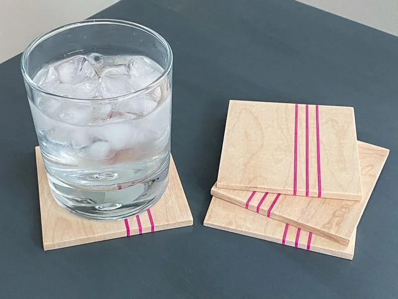 DIY wood coasters with pink stripes on gray table with glass of ice water