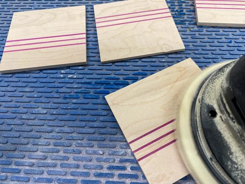 sanding DIY wood coasters on a blue silicone mat