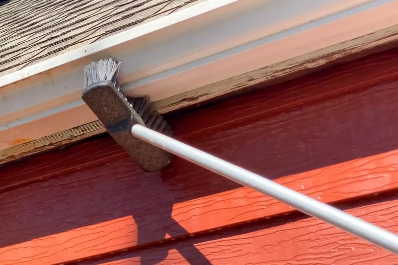 using scrub brush on a pole to clean outside of gutters