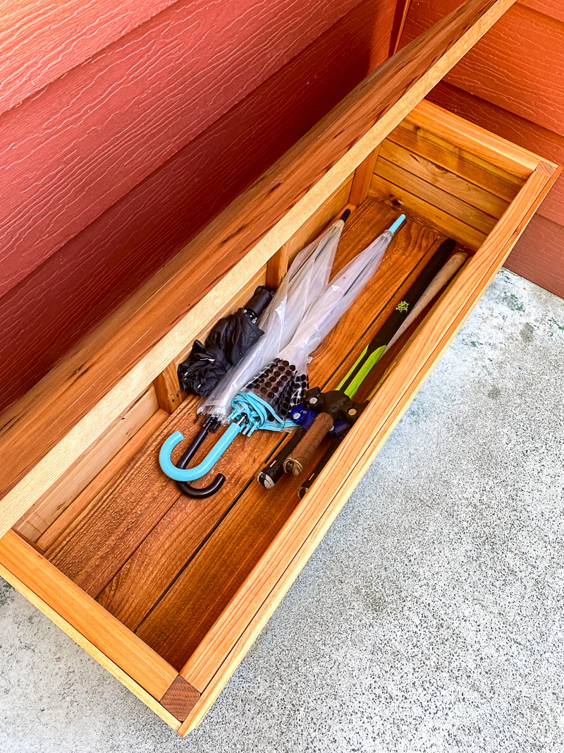 DIY outdoor storage box with lid open, showing umbrellas and toys stored inside