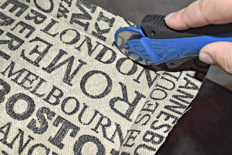 trimming excess fabric around pin board frame with a rotary cutter