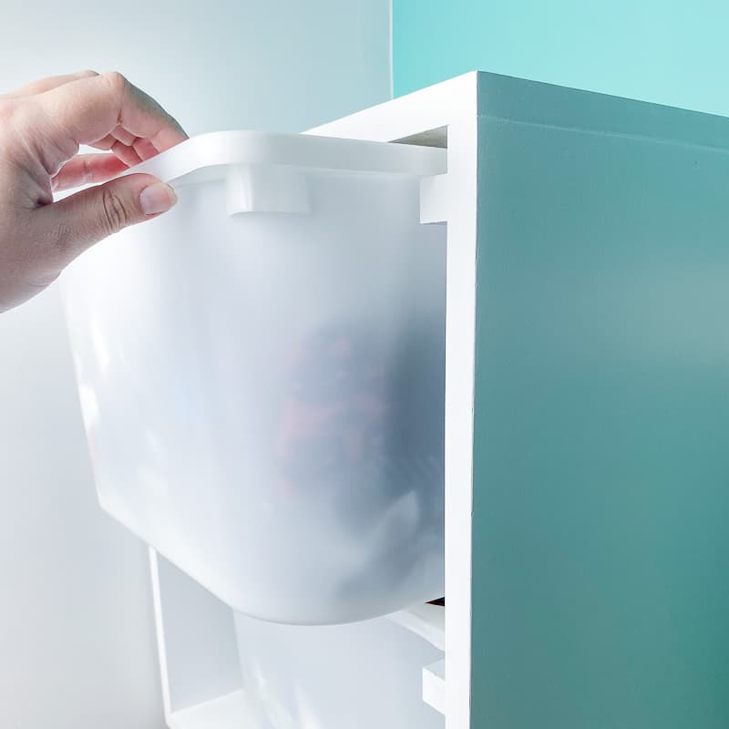 hand pulling out IKEA Trofast bin from wall mounted storage bin frame