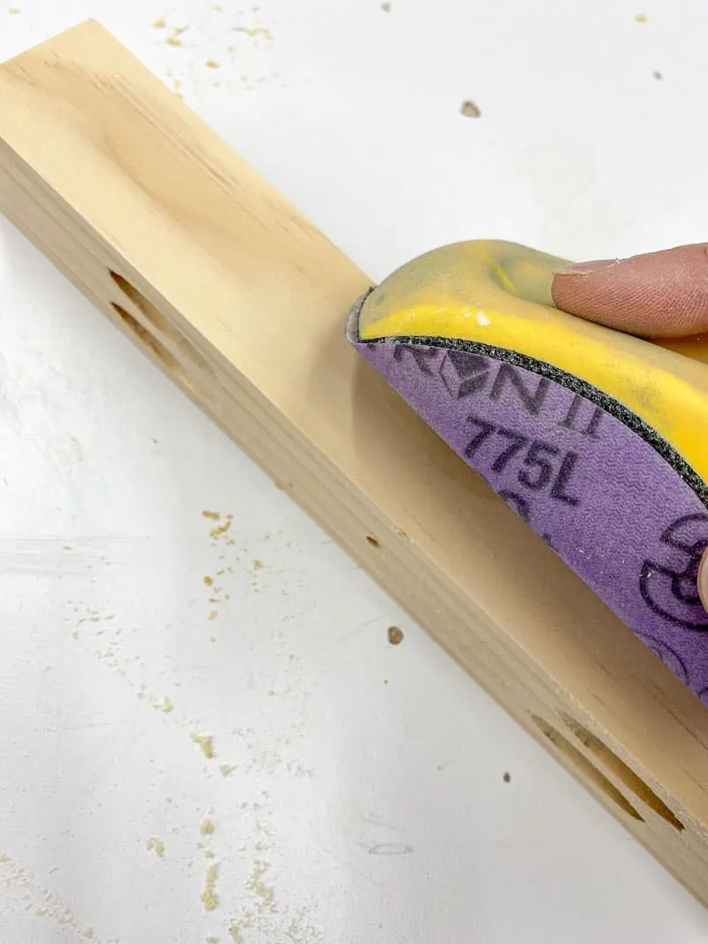 sanding the sharp corners of the 2x2 board with a sanding block