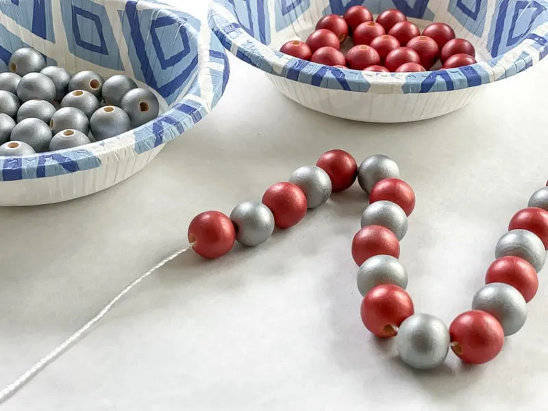 stringing chrome red and silver wood beads on white twine