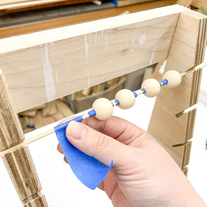 wrapping painters tape around wooden skewer to hold wood beads in place