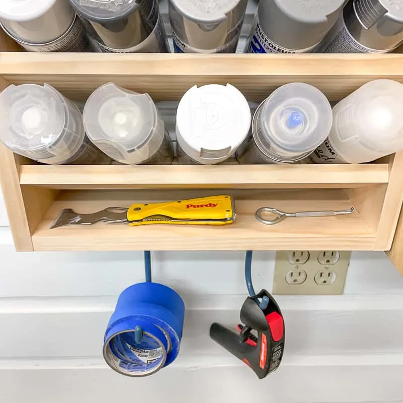 bottom shelf of spray paint storage rack with hooks for painting accessories