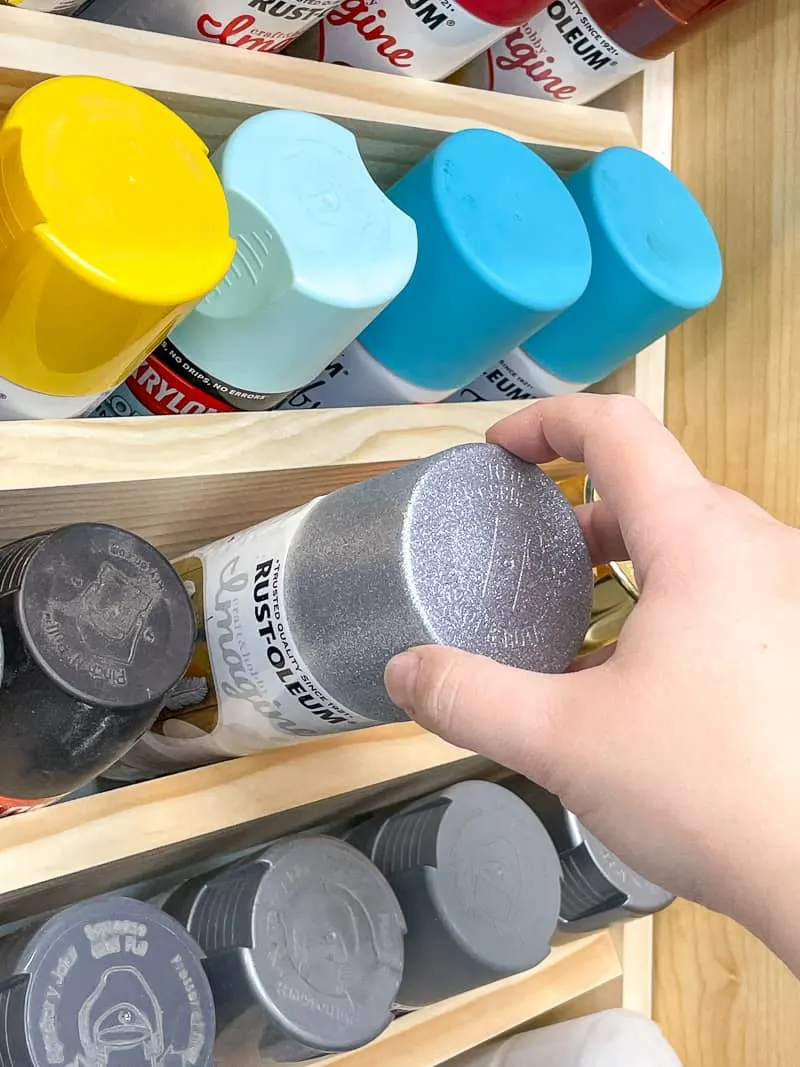 pulling silver glitter spray paint out of spray paint storage rack