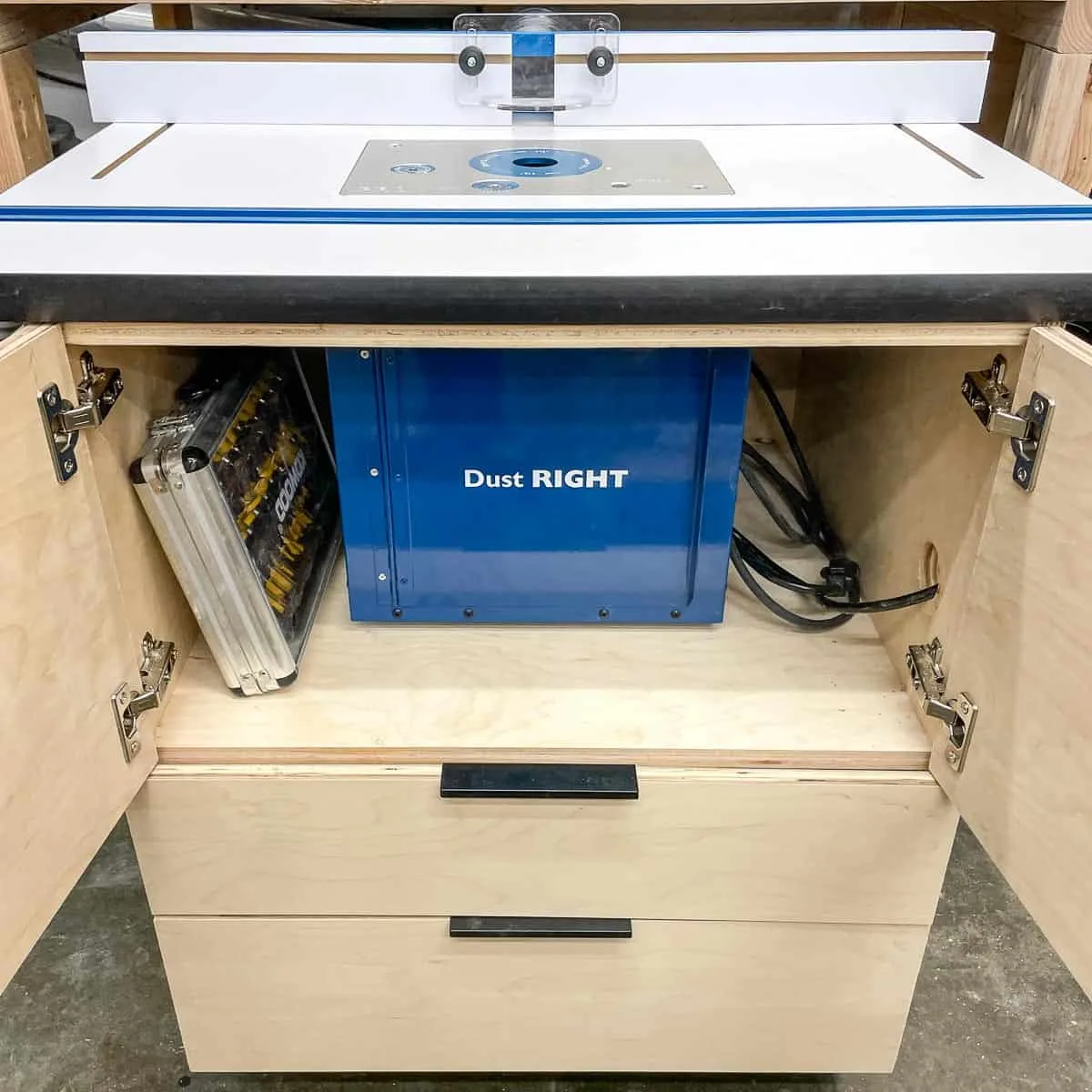 DIY router table with cabinet doors open to reveal dust bucket and router bit set