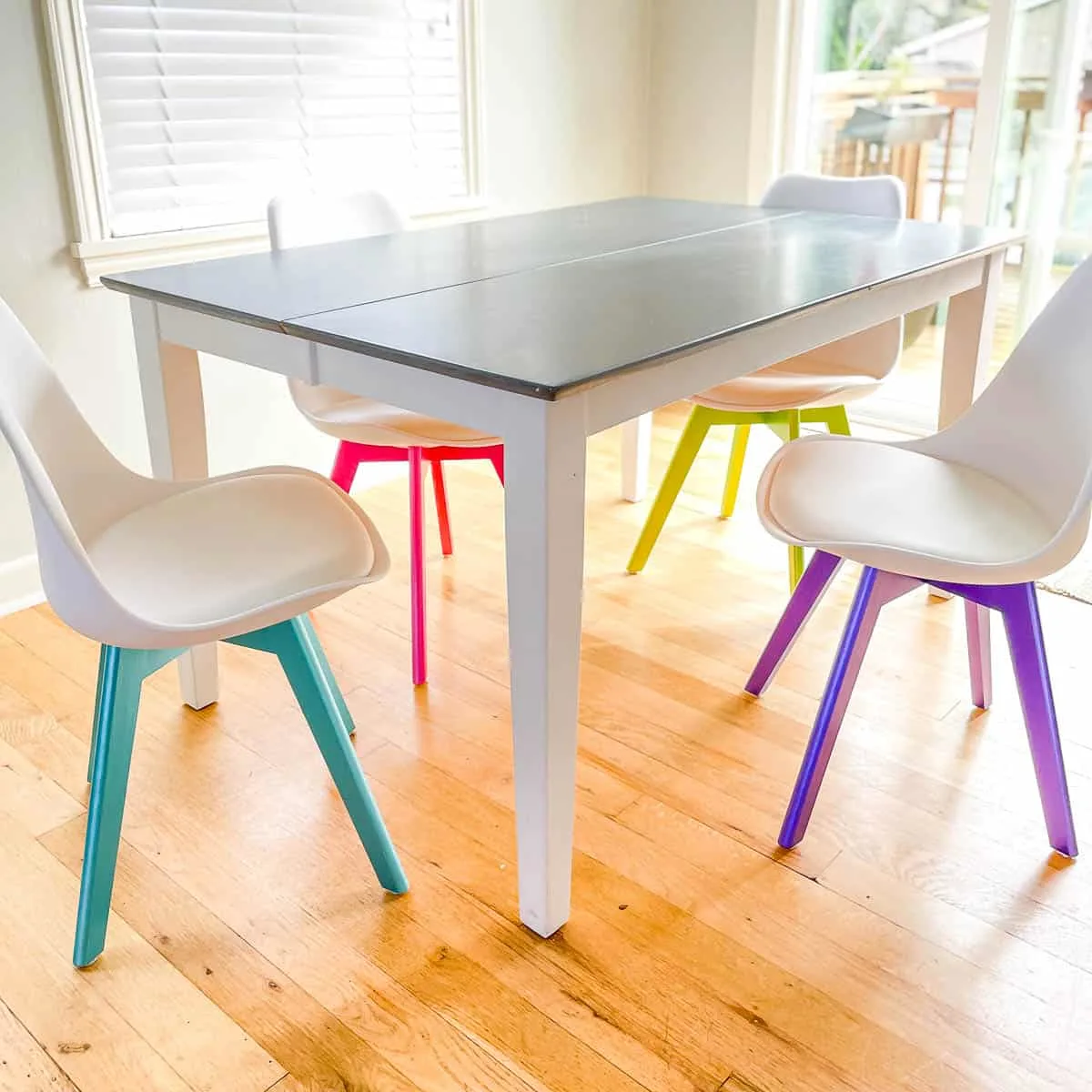 dining room chairs with metallic blue, pink, green and purple bases around a gray and white dining table