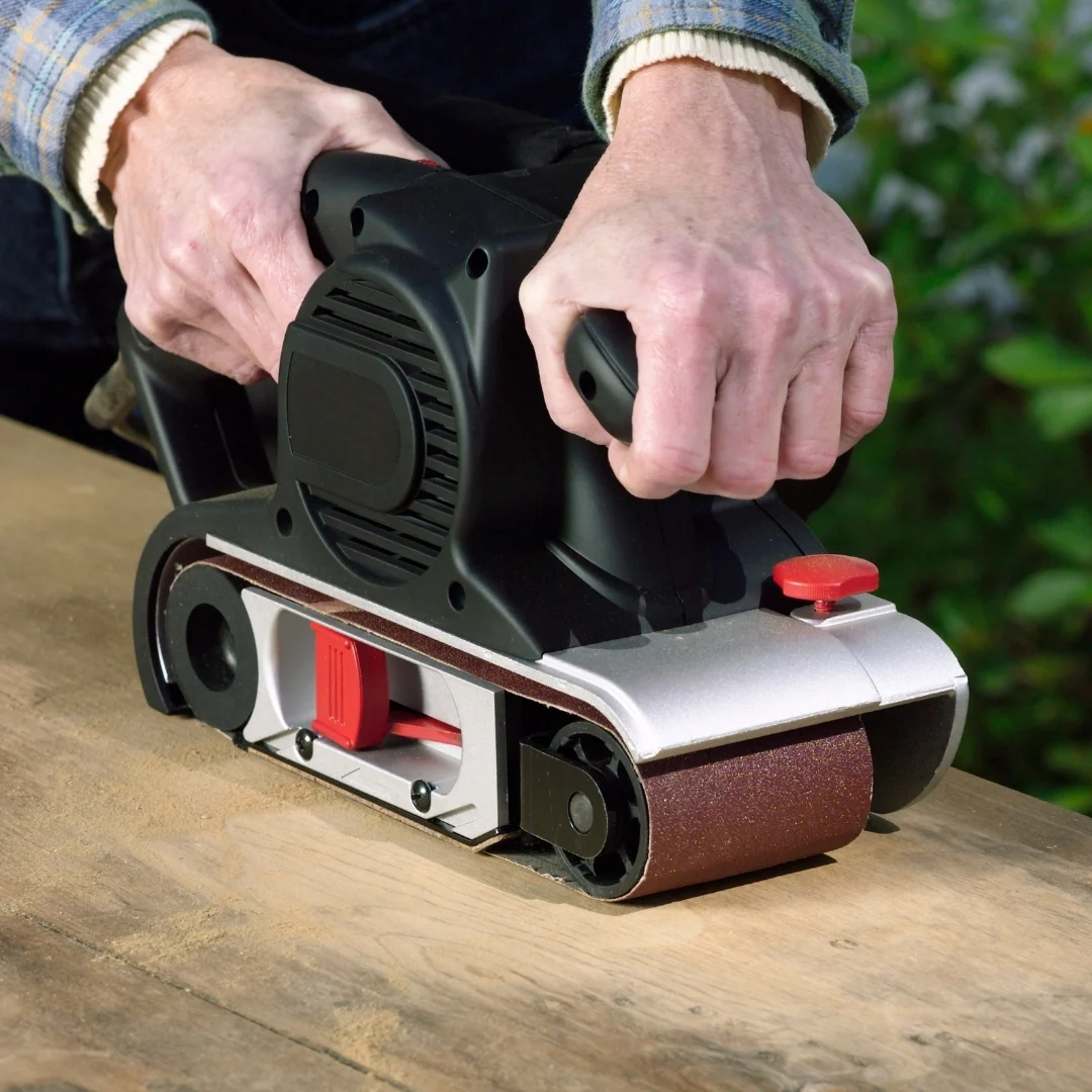 handheld belt sander on rough wood surface