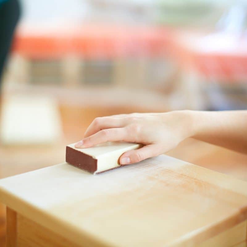 woman's hand sanding wood table top with sanding block