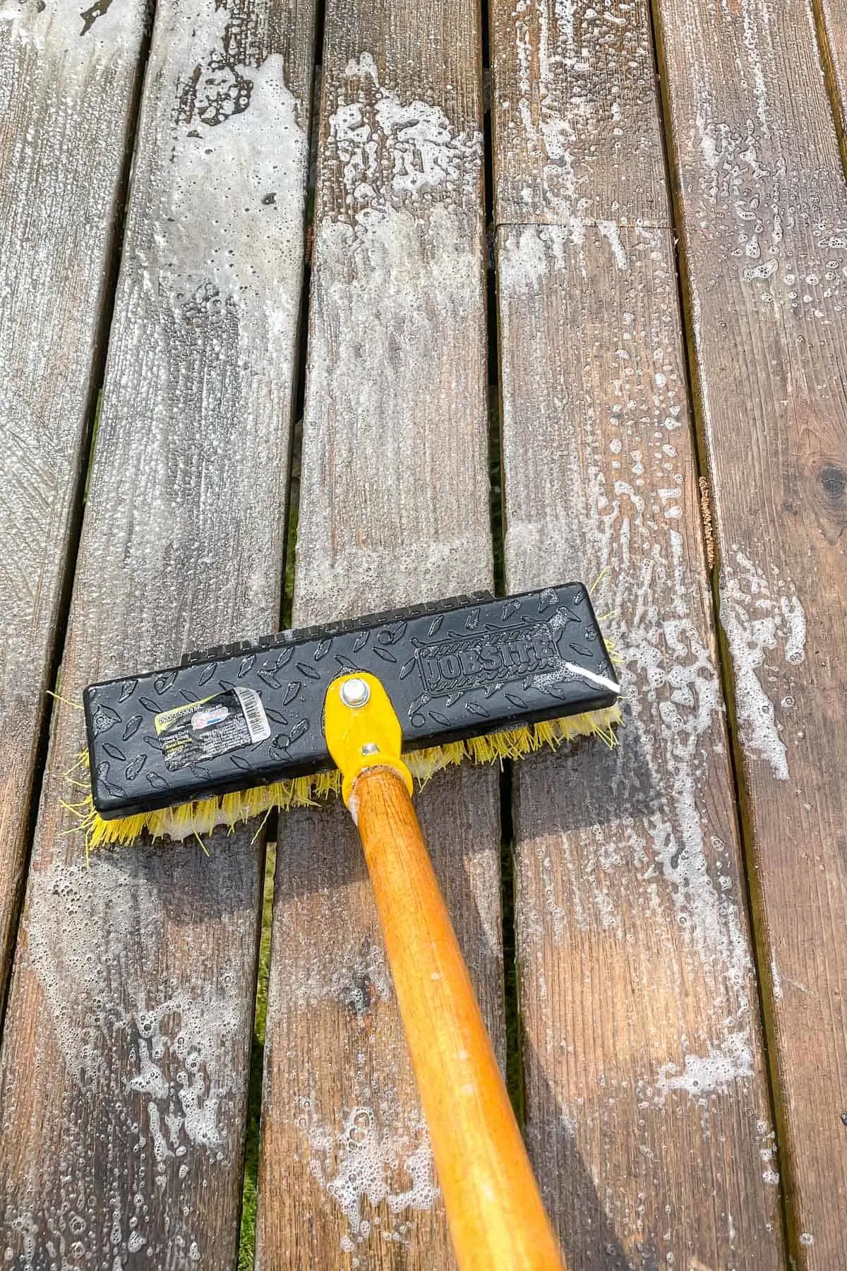 applying deck cleaner to dirty deck with a scrub brush
