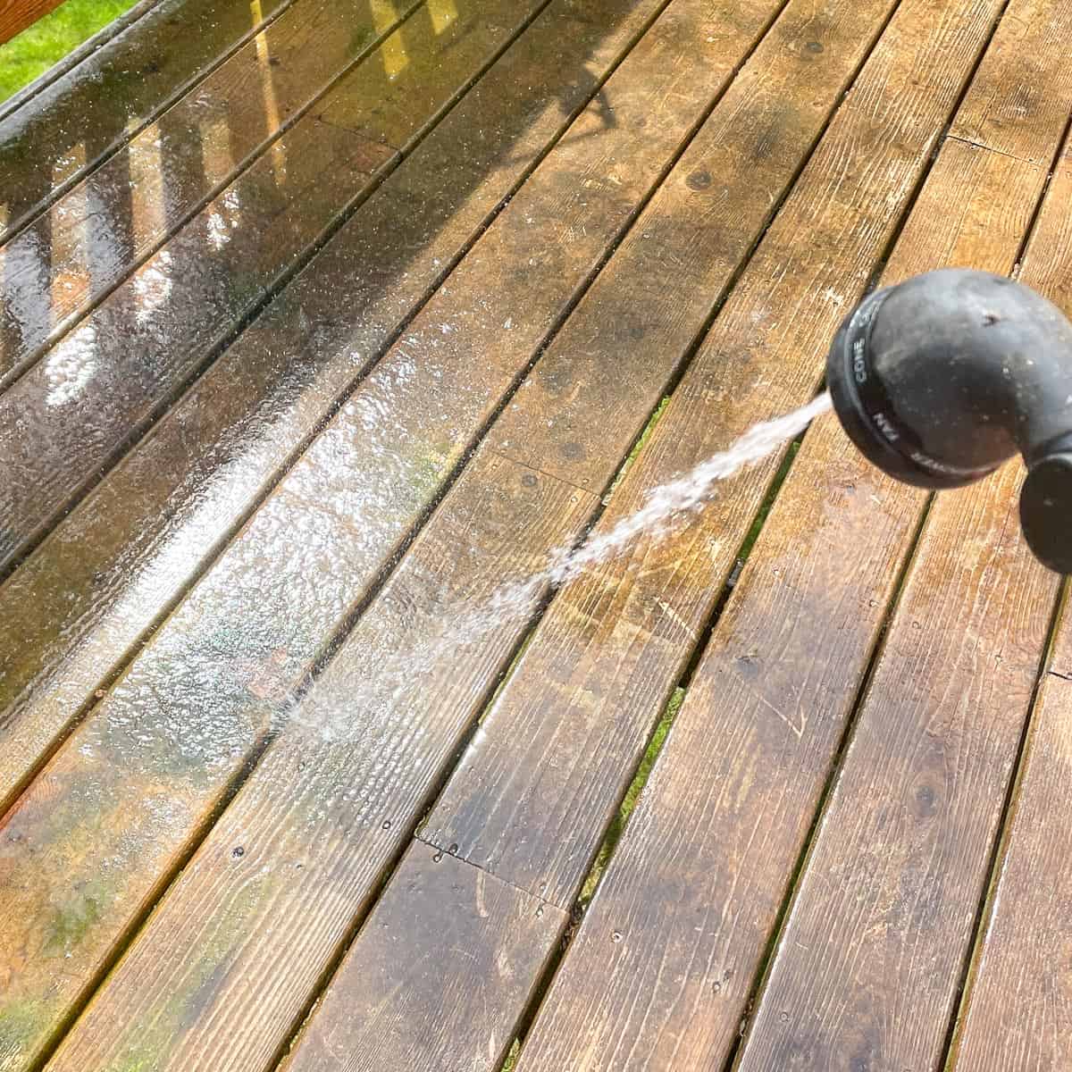 rinsing dirty deck with a hose before cleaning