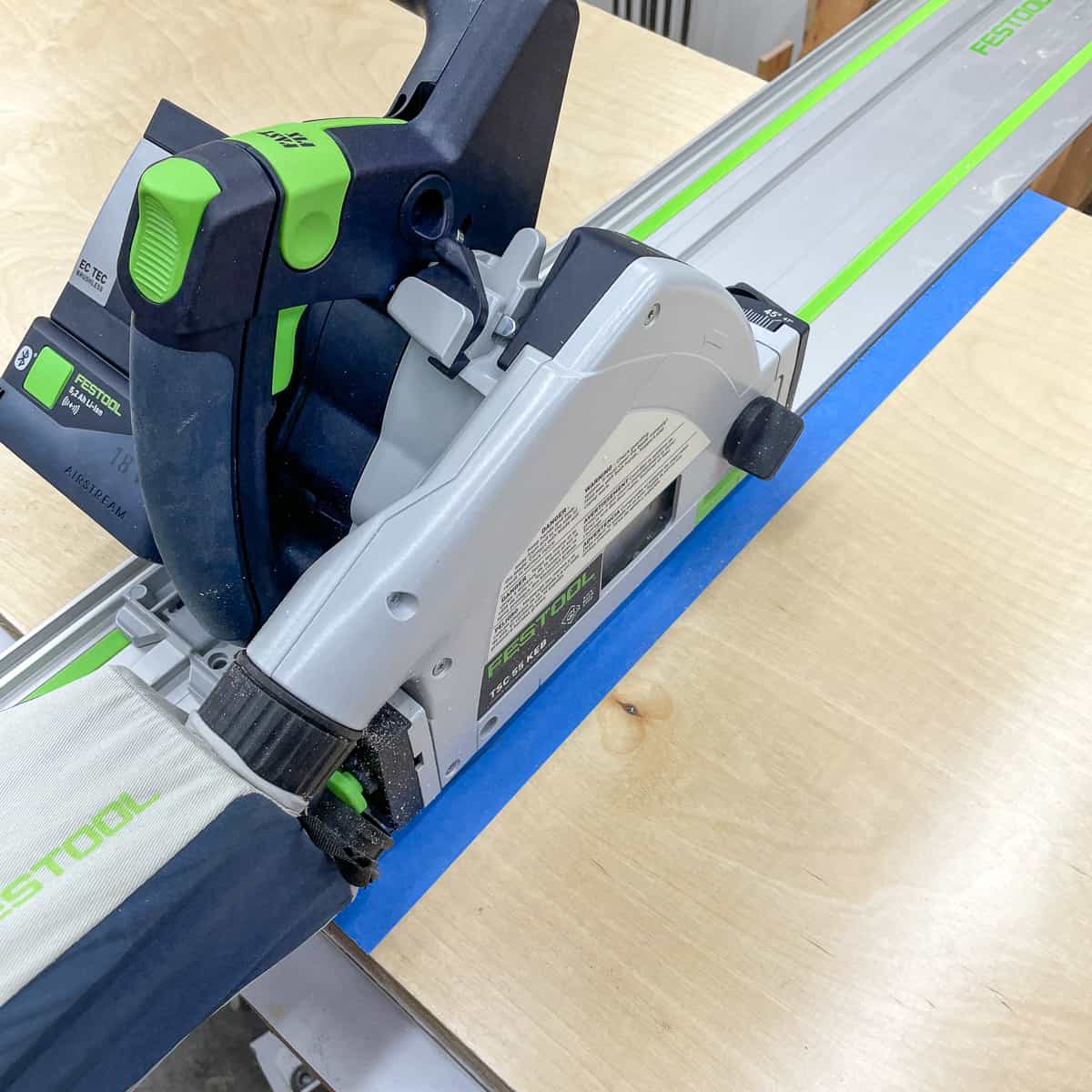 cutting plywood pieces for cabinet box with a track saw with blue painter's tape along the cut line