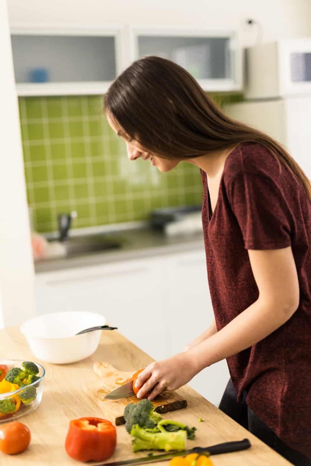 woman standing further back from countertop while chopping vegetables with back bent