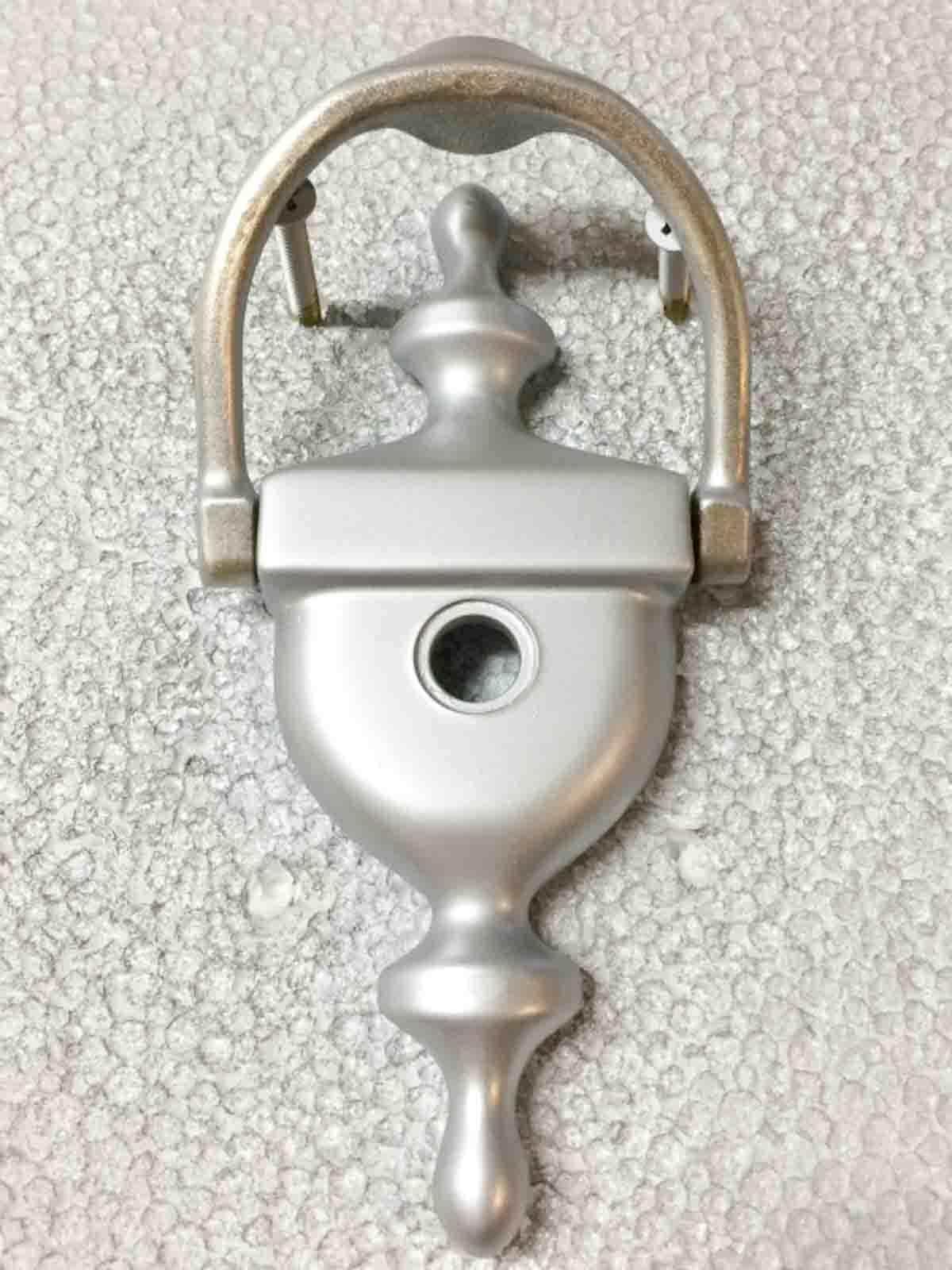 partially spray painted door knocker on styrofoam sheet with screws holding handle off the surface