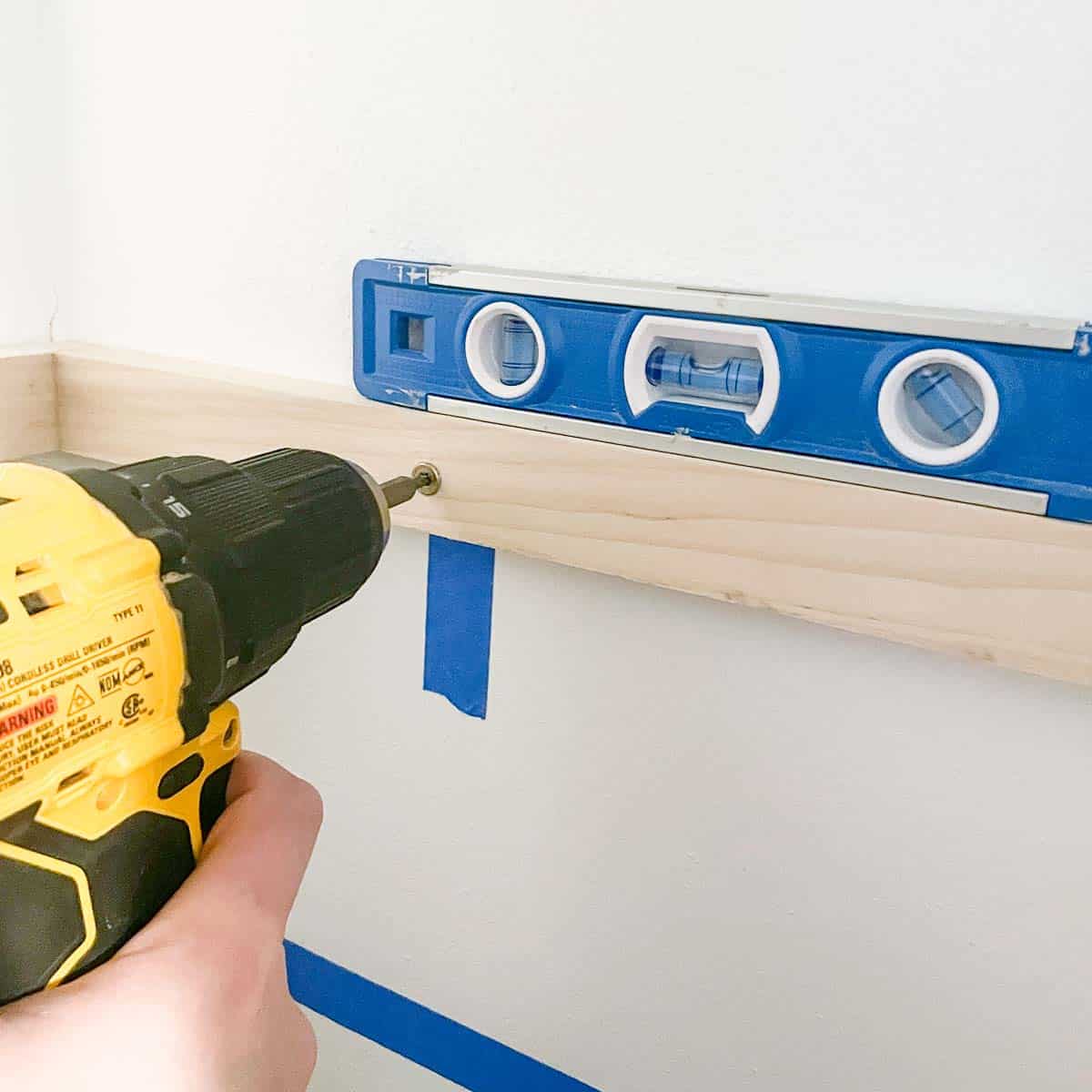 screwing the DIY closet shelf bracket to the wall at the stud with a level on top