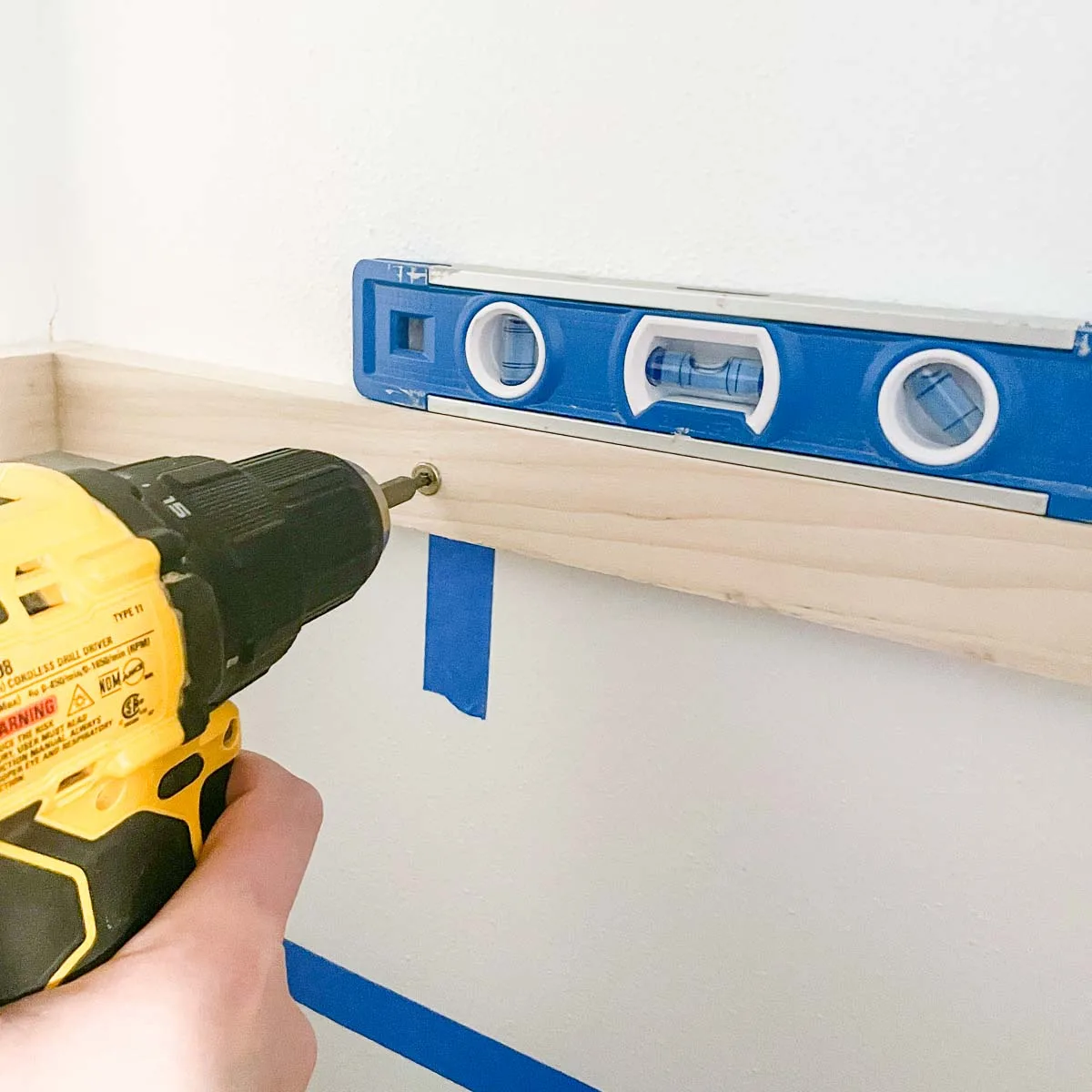 screwing the DIY closet shelf bracket to the wall at the stud with a level on top