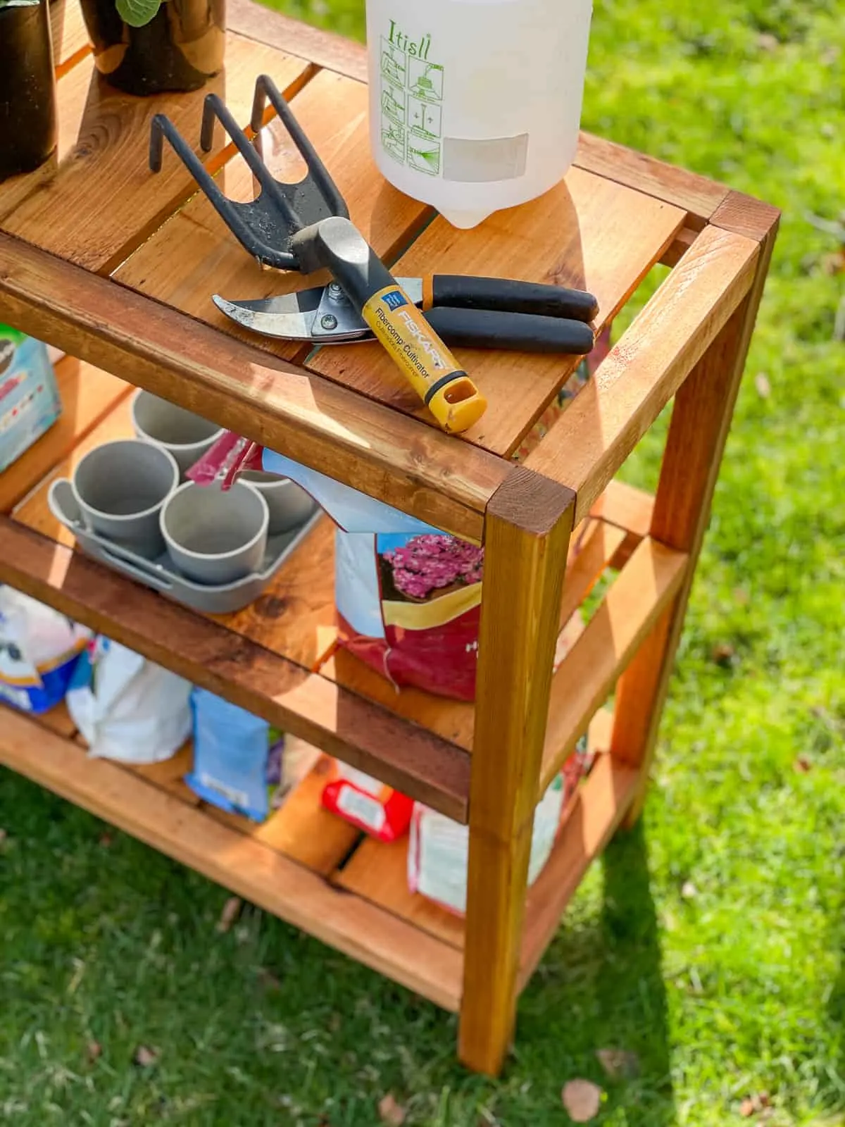 pruners and gardening tools on top shelf of DIY outdoor shelves, with pots and bags of fertilizer below