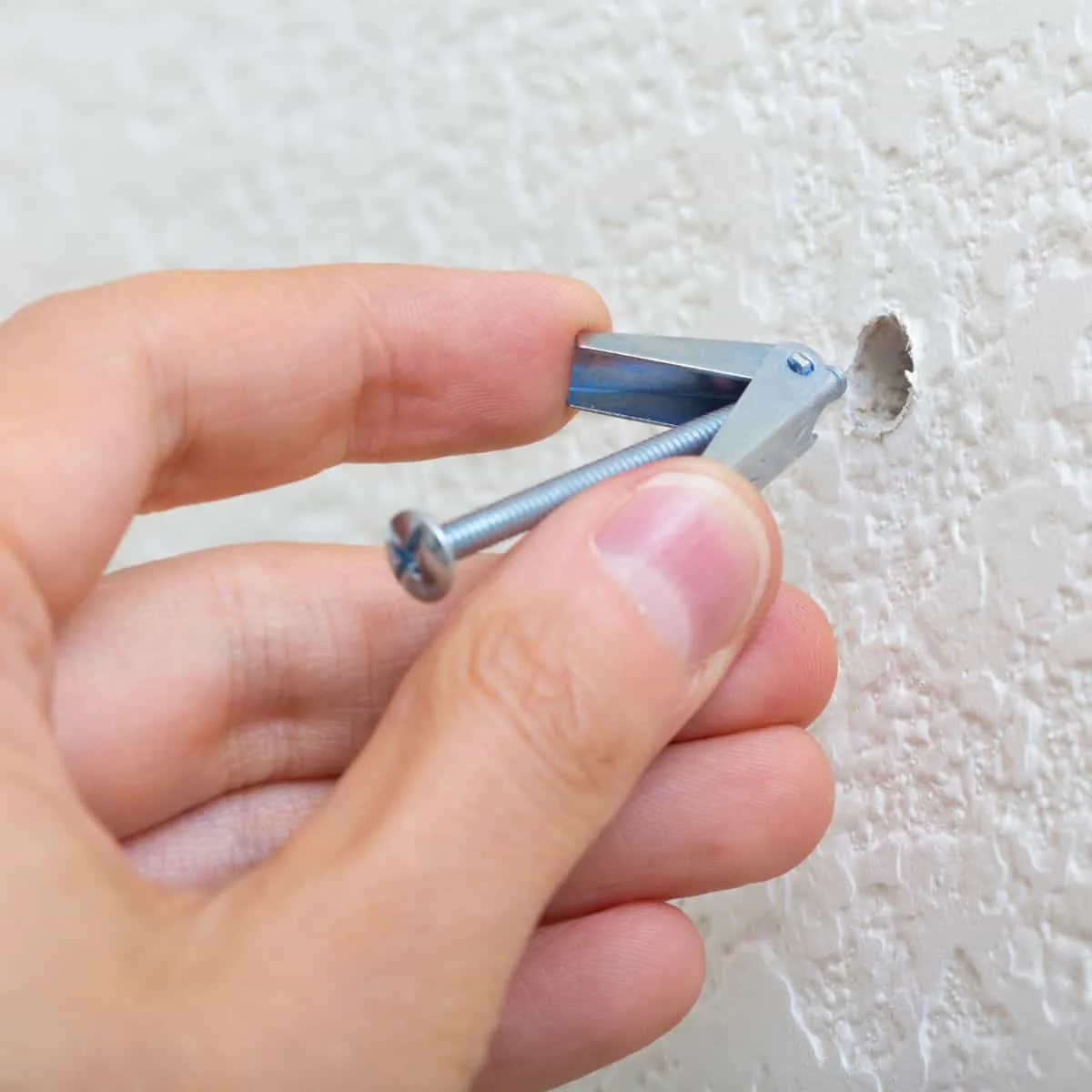 inserting toggle bolt into a hole in the wall