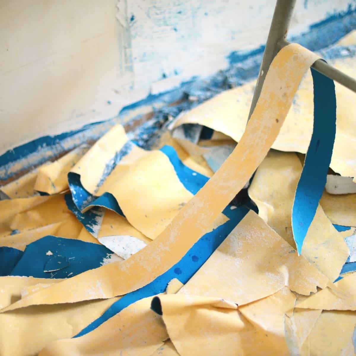 strips of wallpaper peeled off the wall and on the floor