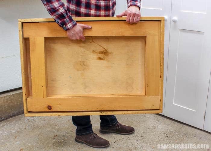 Man holding DIY folding workbench folded up to store away.
