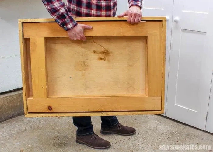 Man holding DIY folding workbench folded up to store away.