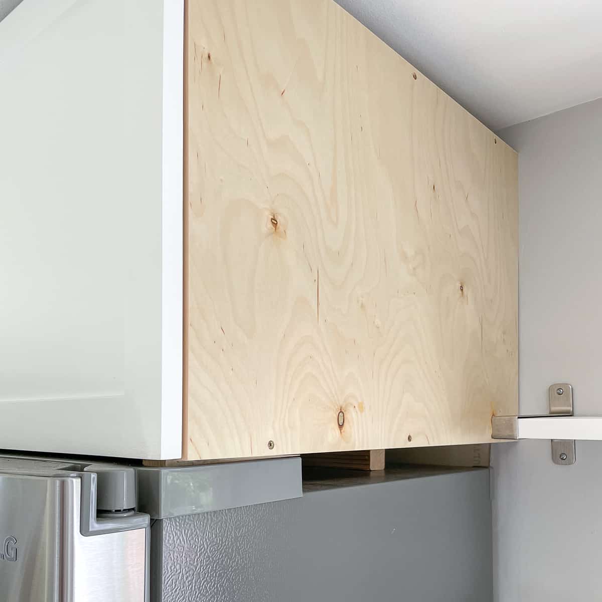 scrap wood block propping up back of cabinet above fridge