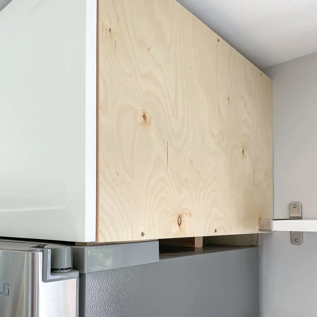 scrap wood block propping up back of cabinet above fridge