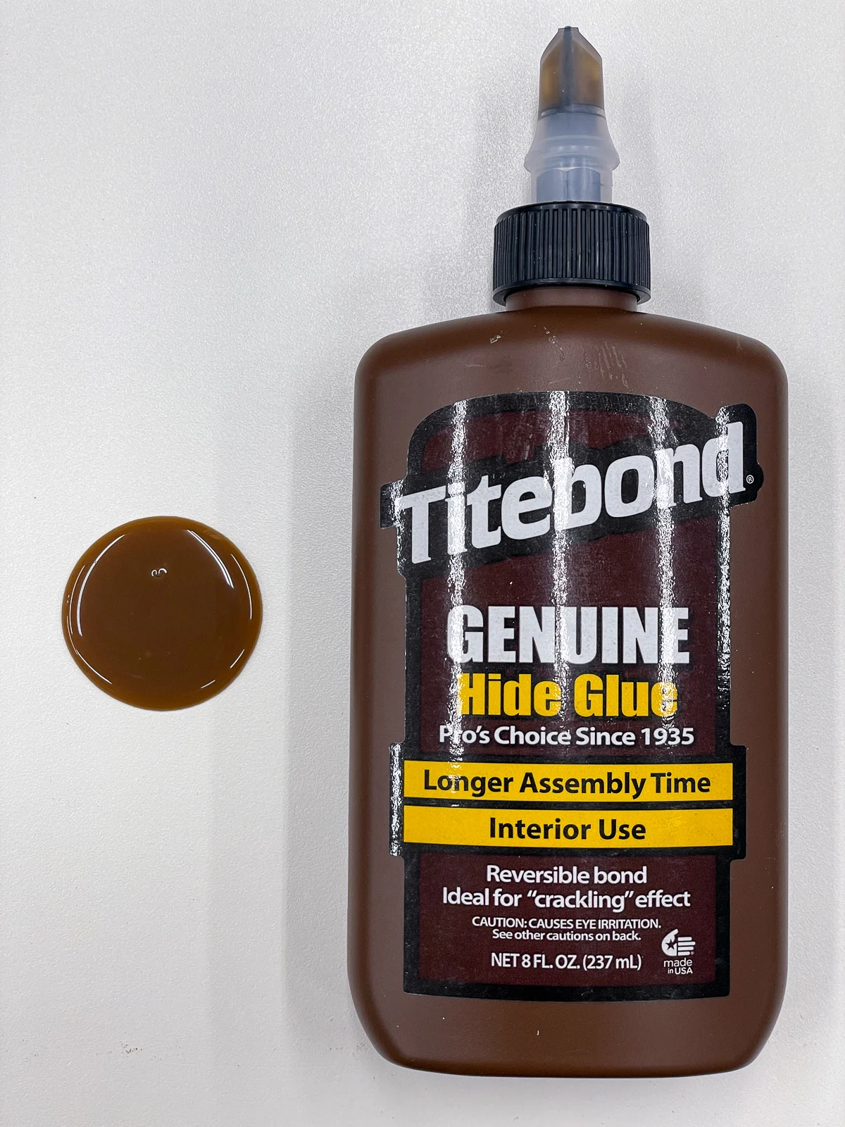 bottle of hide glue next to puddle of hide glue on melamine board
