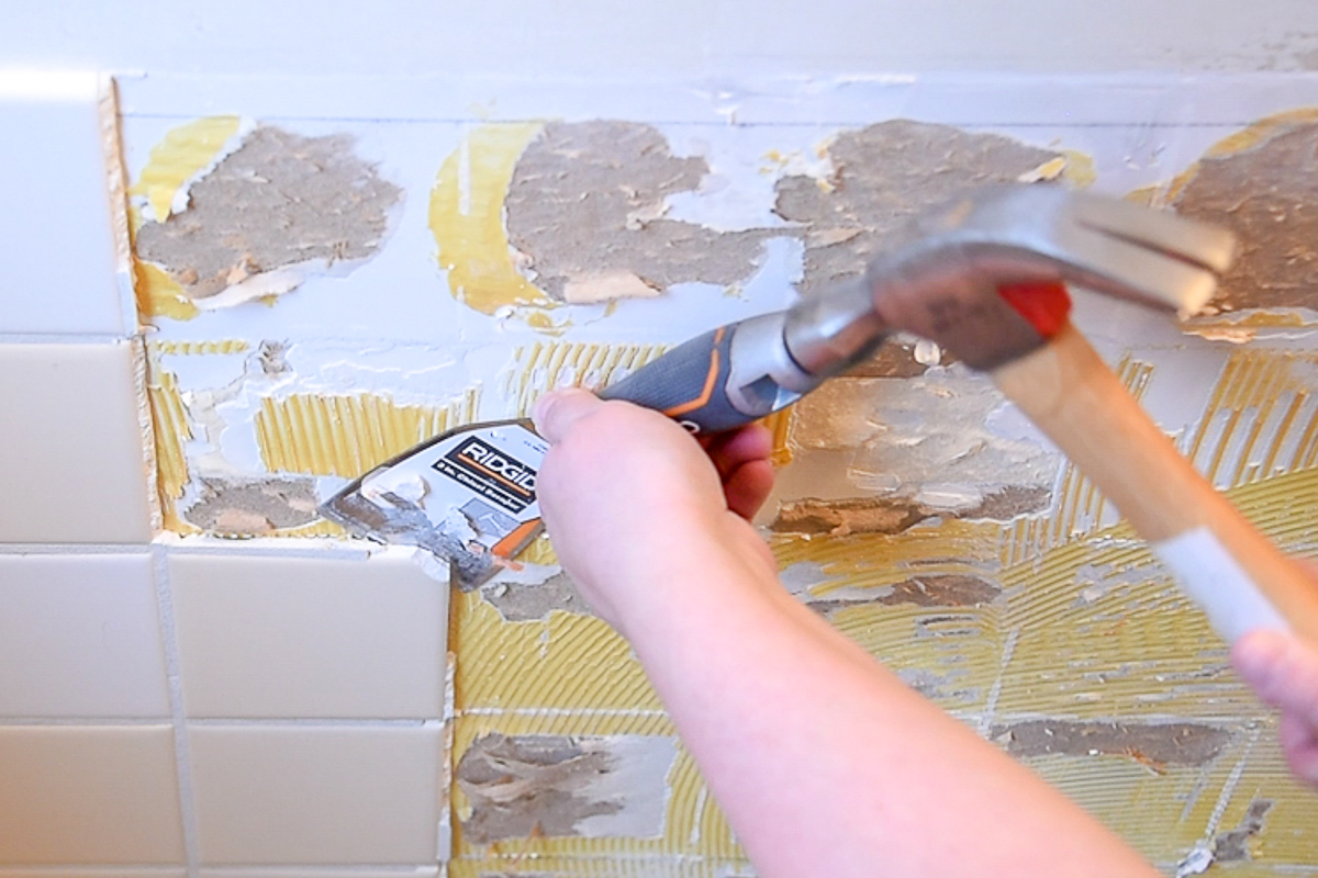 using a bent scraper tool and a hammer to remove wall tile