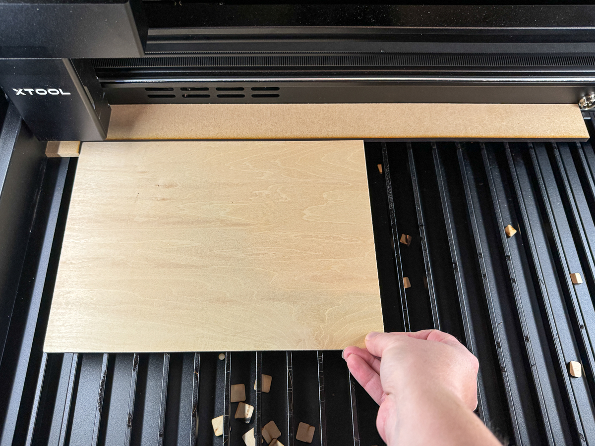 placing plywood into the xTool P2 laser cutter bed with a jig to ensure proper alignment