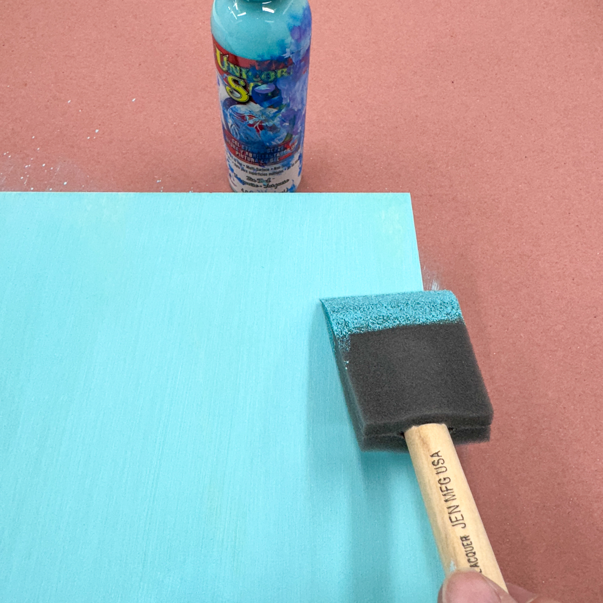 applying aqua unicorn spit stain to a plywood board with a foam brush