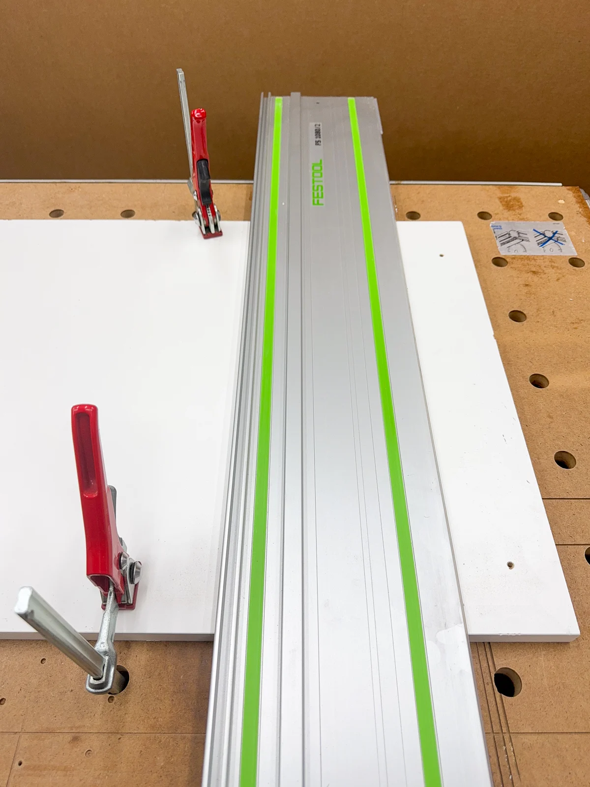 sheet of white melamine clamped down to the workbench with a track for the saw on top