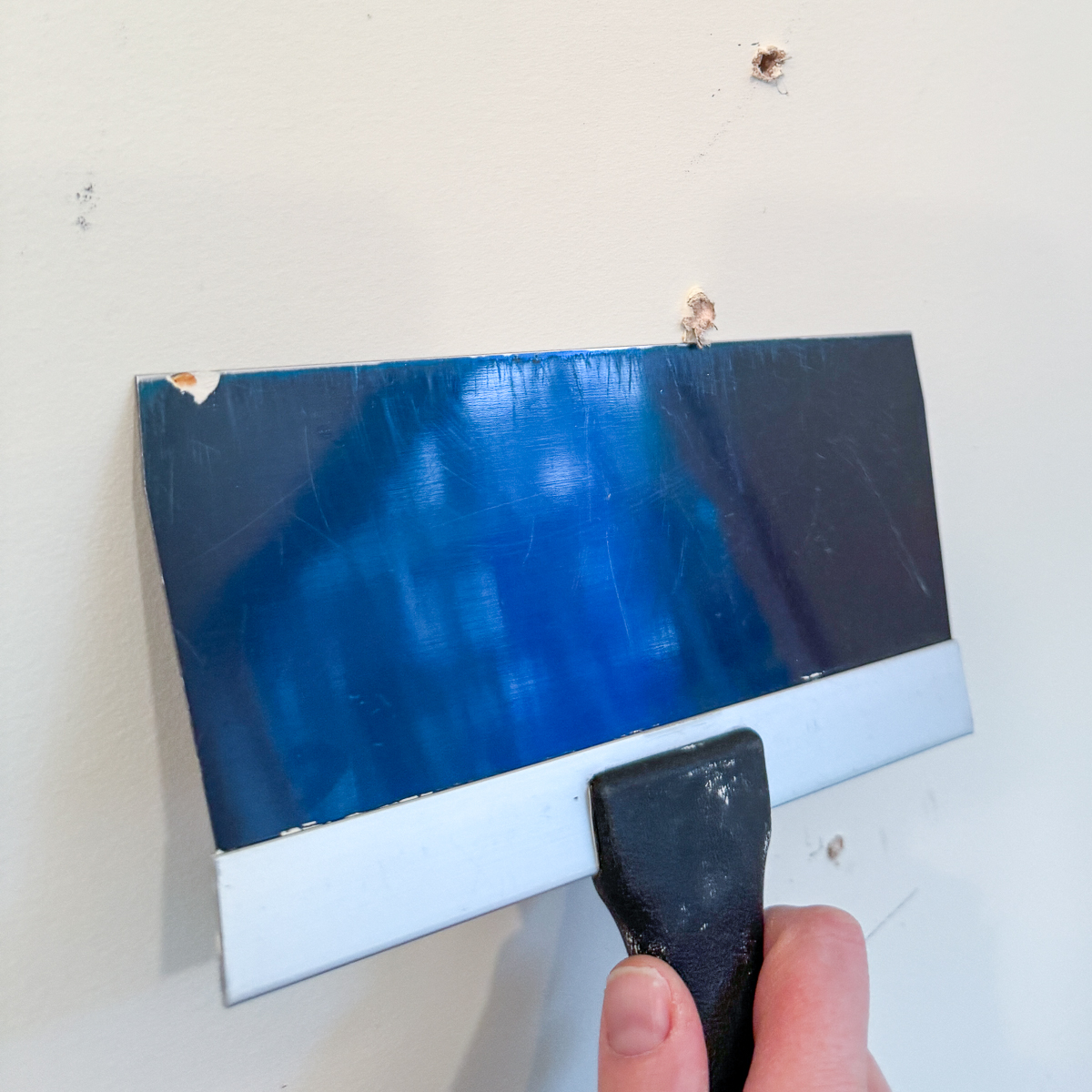 using a drywall knife to knock down high spots around hole