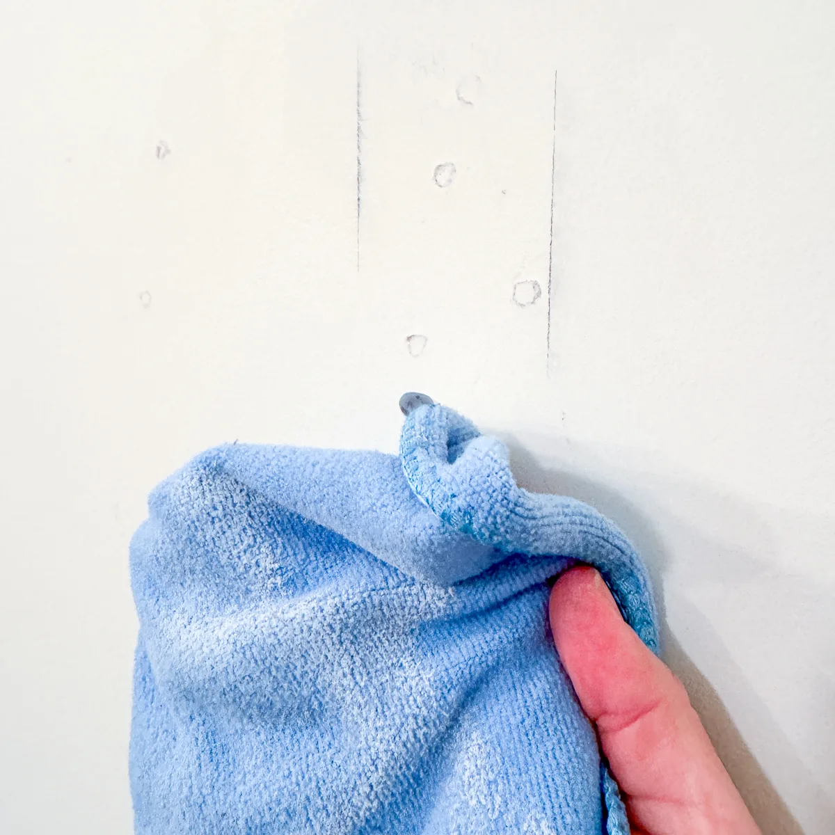 removing dust from the wall with a blue microfiber cloth after sanding down spackle
