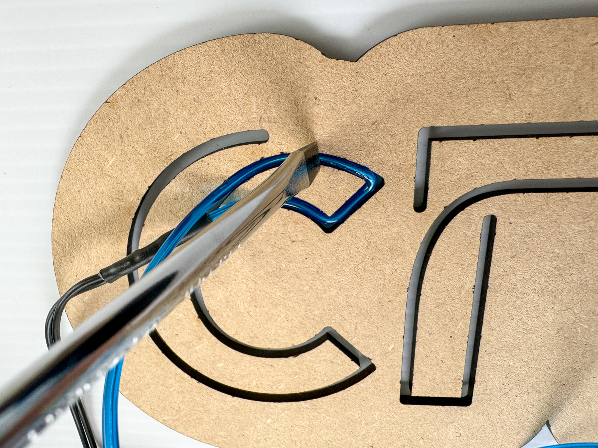 pressing EL wire into a DIY neon sign with a flat head screwdriver