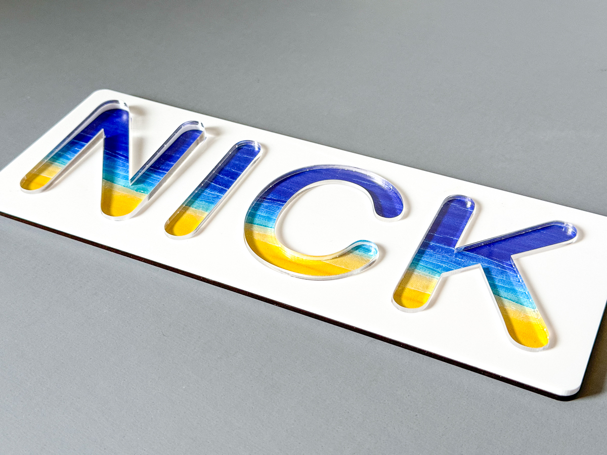 white acrylic name puzzle with patterned acrylic backer and clear letters spelling out NICK