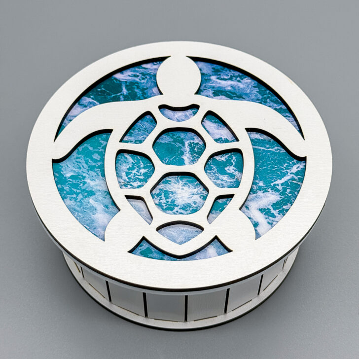 round wood box with white silhouette of a sea turtle over an ocean wave pattern